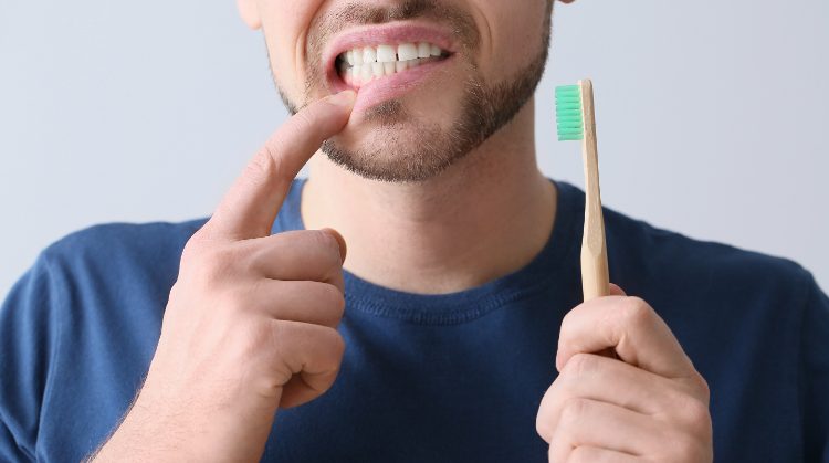 Man pointing to bleeding gums while holding a toothbrush – Dental Nation, Las Vegas, NV